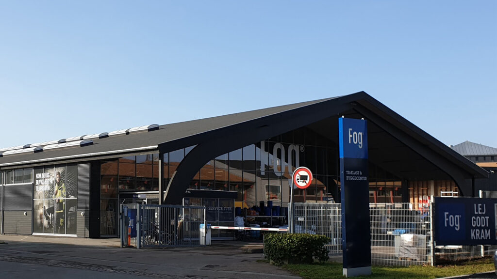 Utvendig bilde av Johannes Fog trelast- og byggesenter i Herlev, Danmark, med skilt og inngang.