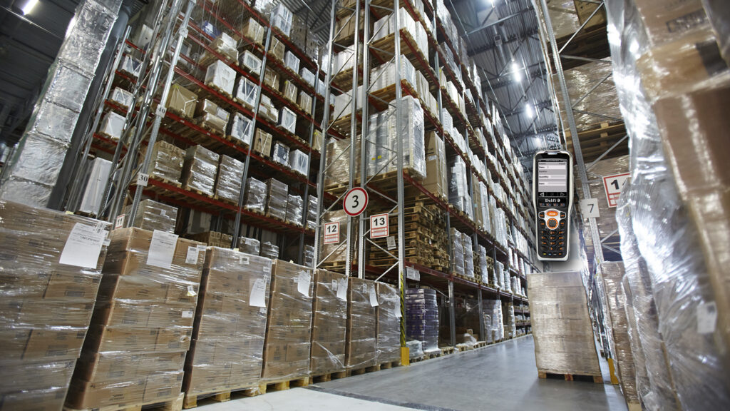 Digitales Handheld-Terminal in einem Lager mit hohen Regalen voller verpackter Waren.