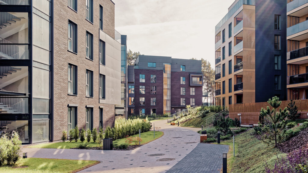 Edifici residenziali moderni con appartamenti e balconi, e un percorso pavimentato circondato da vegetazione.