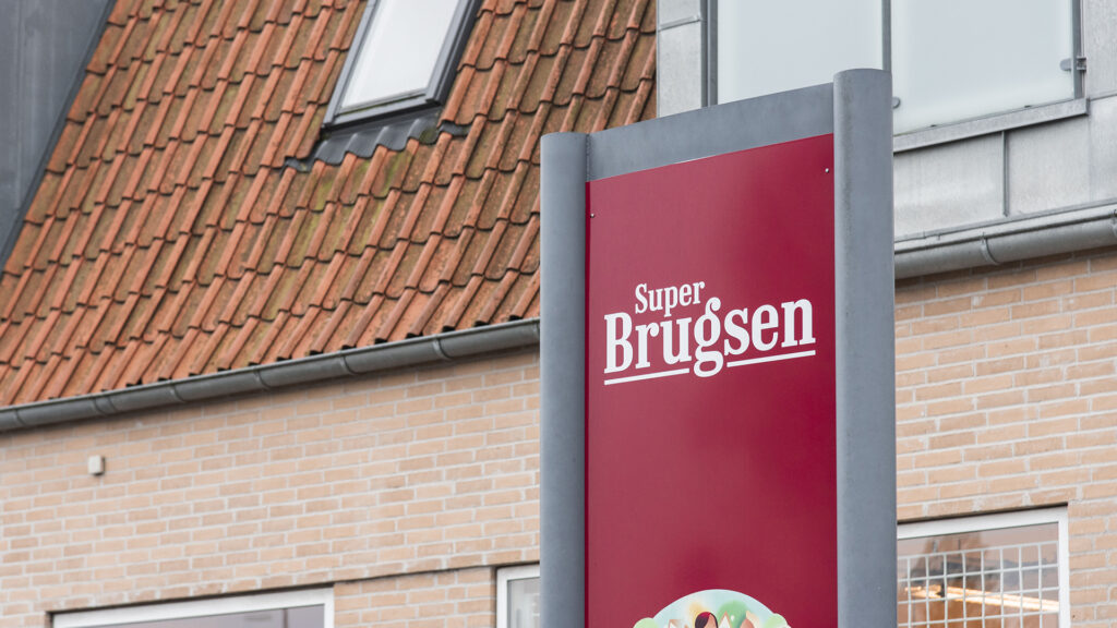 SuperBrugsen-skilt foran mursteinsbygning med oransje takstein og vinduer.