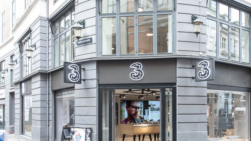 Bygningshjørne med en 3-butikk og store vinduer som viser digitale skilting innendørs.