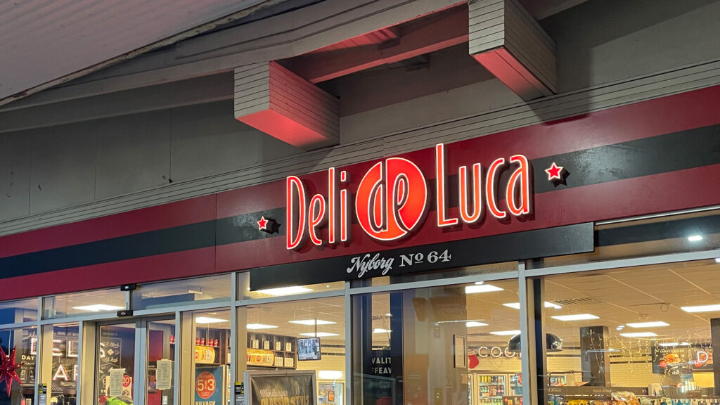 Lysrörsskylt för Deli de Luca Nyborg Nº 64 över butiksentrén.