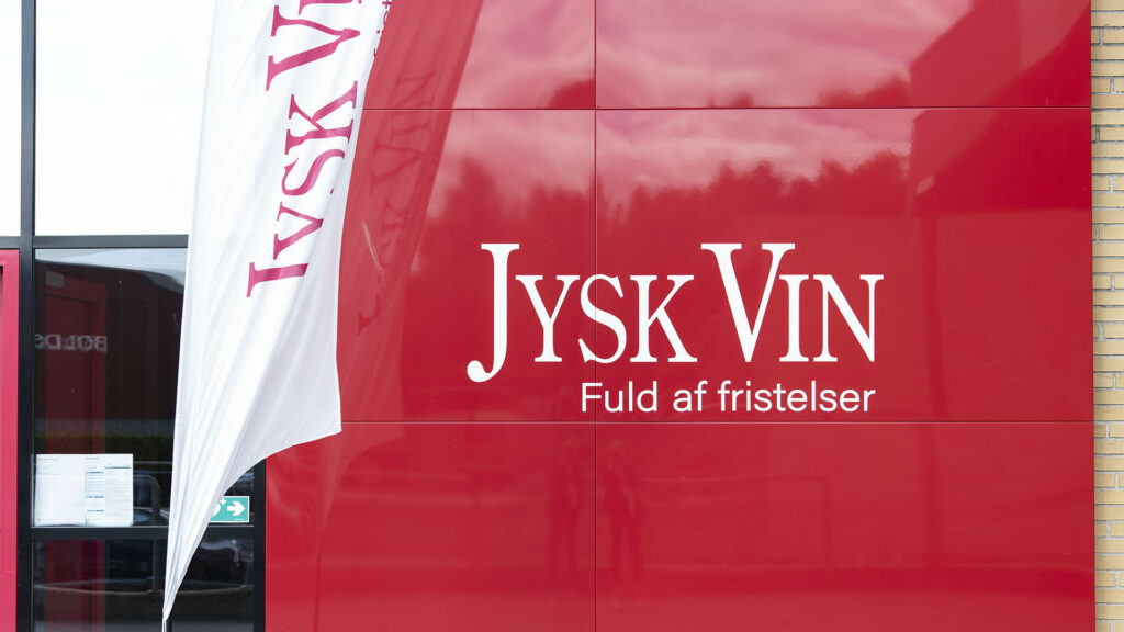 Jysk Vin Ladenfront mit rotem Schild und weißer Aufschrift, daneben eine weiße Flagge.
