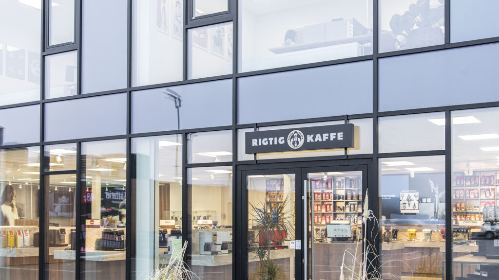 Außenansicht des Rigtig Kaffe Showrooms mit Logo, großen Fenstern und Kaffeemaschinen.