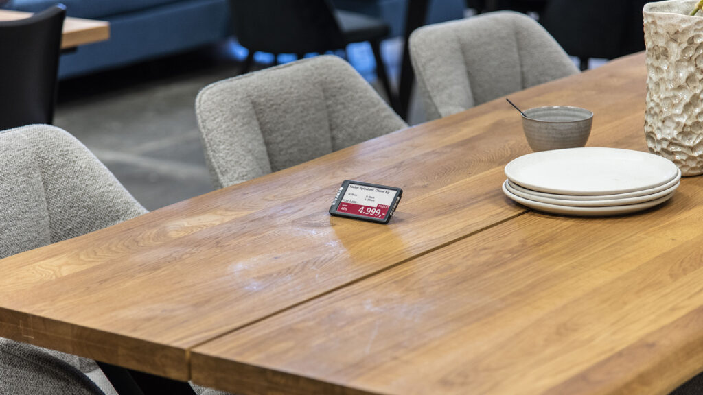Digitales Preisschild auf einem Holztisch in einem Möbelausstellungsraum.