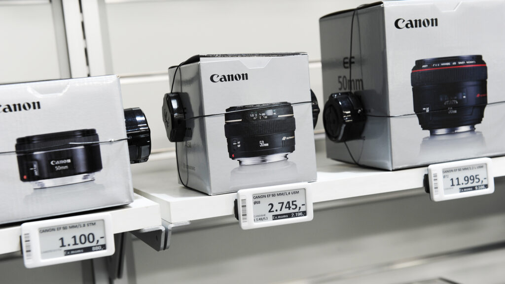 Elektronische Regaletiketten zeigen Preise und Informationen für Canon Kameraobjektive in einem Goecker-Geschäft.