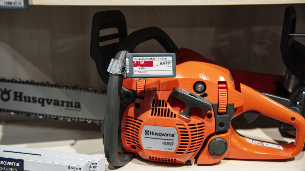 Orange Husqvarna motorsav med digitalt prisskilt i en butiksudstilling.