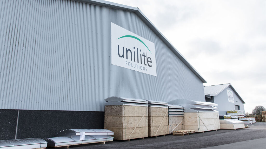 Unilite lagerbygning med firmalogo, trækasser og ovenlysvinduer på paller.