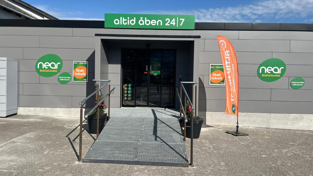 Exteriör av Near livsmedelsbutik med ramp och digital skyltning.