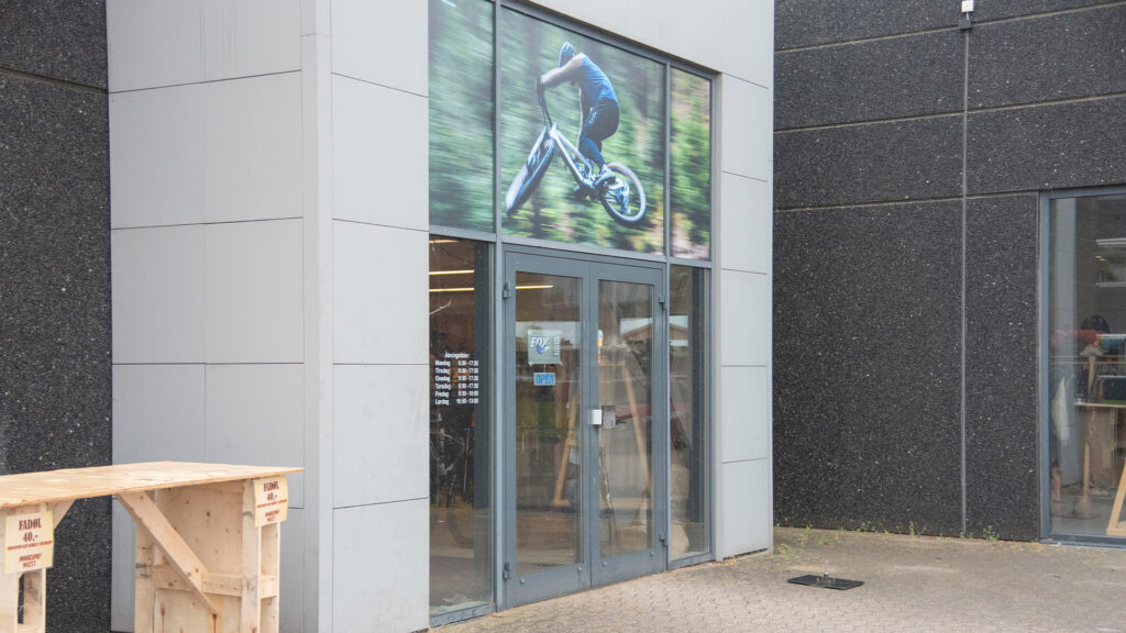 Eingang von Cycle Sport Silkeborg mit einem Poster eines Mountainbikers darüber.