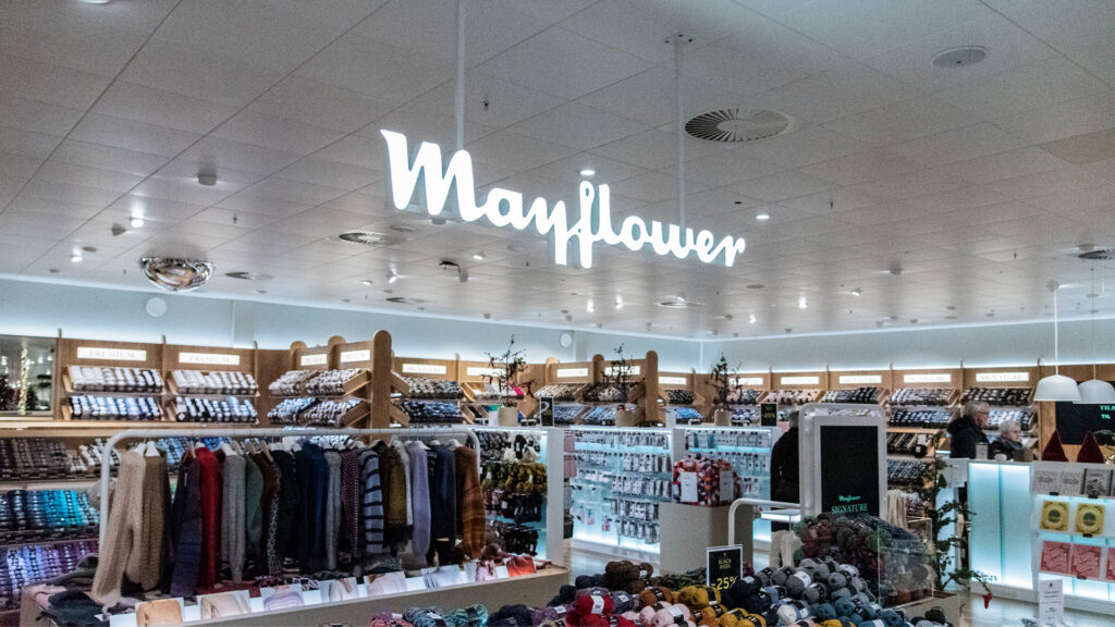 Beleuchtetes Mayflower-Schild in einem Geschäft mit Garn und Kleidung auf digitalen Preisschildern.
