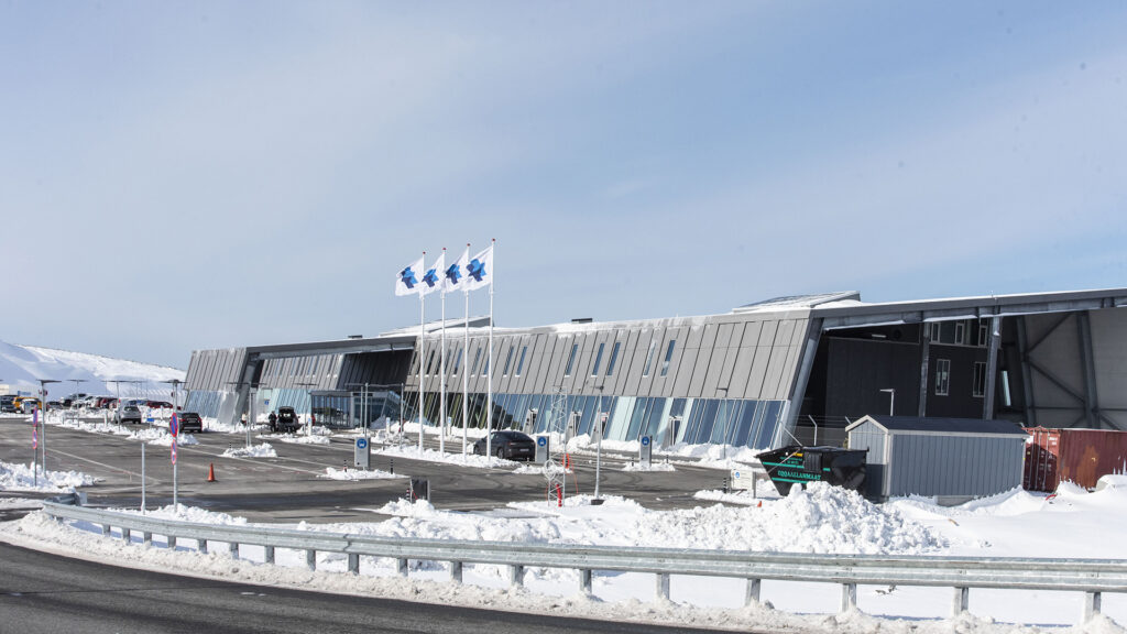 Flughafen Nuuk mit moderner Architektur, Parkplatz und Schnee, drei Flaggen.